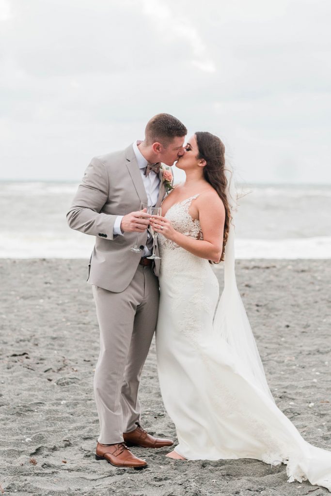couple shares a kiss and champagne toast for beach wedding